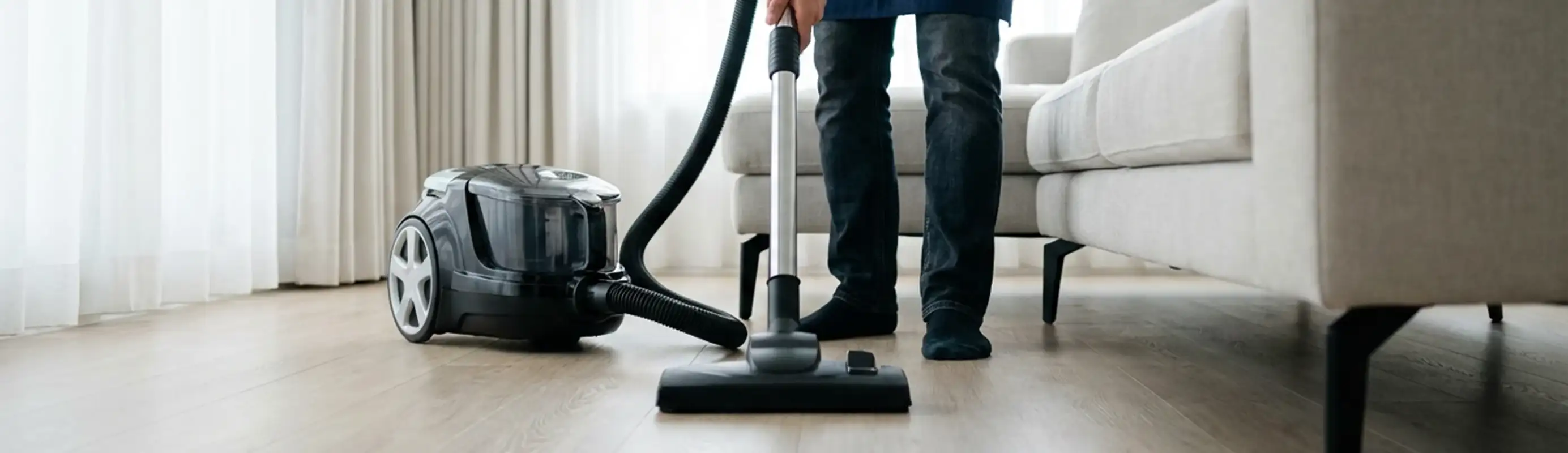 Professional house cleaner vacuuming a living room floor with a canister vacuum cleaner, Boise, ID.