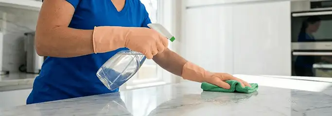 Maid service worker spraying and wiping a kitchen countertop with a microfiber cloth for sanitizing, Boise, ID.