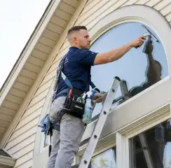 Professional window cleaner on a ladder using a squeegee to clean an exterior arched window, Boise, ID.