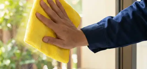 House cleaner wiping a glass window with a yellow microfiber cloth for streak-free cleaning, Boise, ID.